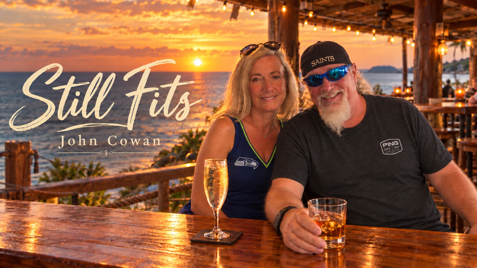 John and Ginny smiling together at a coastal bar with whiskey and champagne at sunset